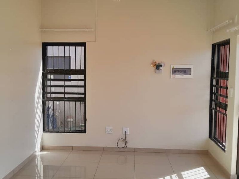 A bright, empty living area featuring polished tiled flooring, security bars on windows, and a central pendant light fixture.