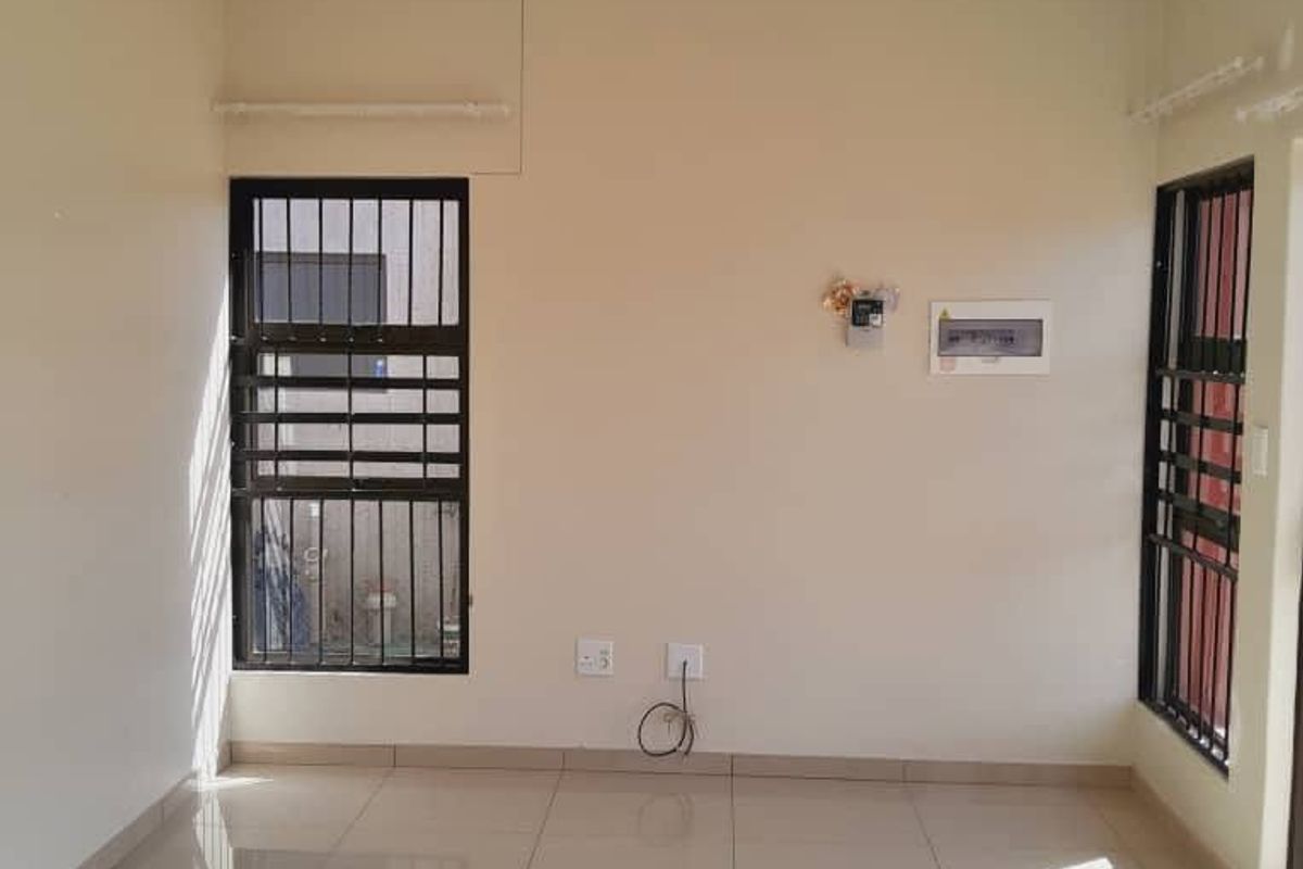 A bright, empty living area featuring polished tiled flooring, security bars on windows, and a central pendant light fixture.