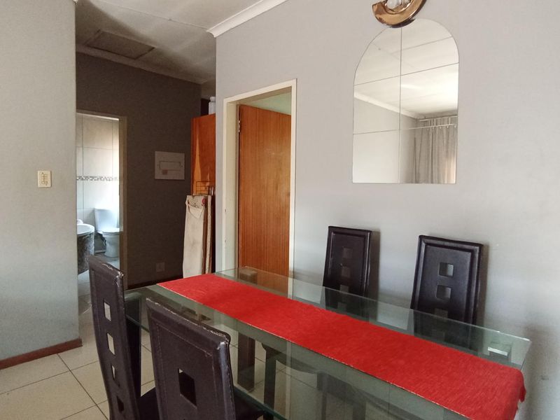 A dining area featuring tiled flooring and a wall-mounted mirror, with an adjacent view into a bathroom space.
