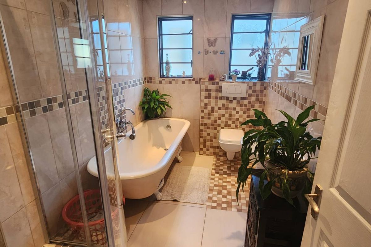 A functional bathroom featuring a clawfoot bathtub, a separate glass-enclosed shower, and a wall-mounted toilet with mosaic tile accents.