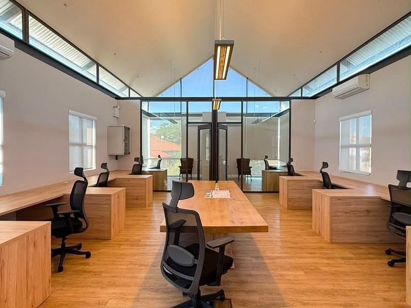 Modern open-plan office space featuring vaulted ceilings, clerestory windows, integrated wooden workstations, and high-quality laminate flooring with excellent natural light.