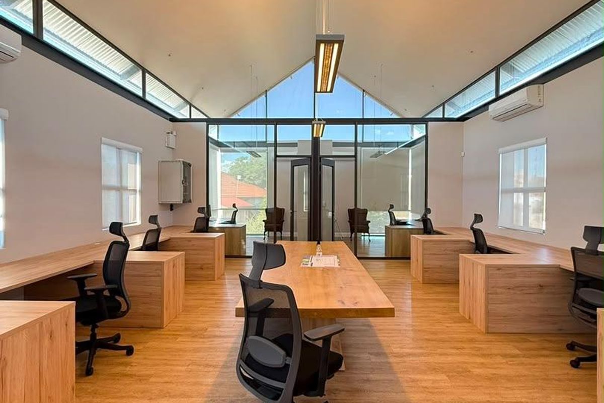 Modern open-plan office space featuring vaulted ceilings, clerestory windows, integrated wooden workstations, and high-quality laminate flooring with excellent natural light.
