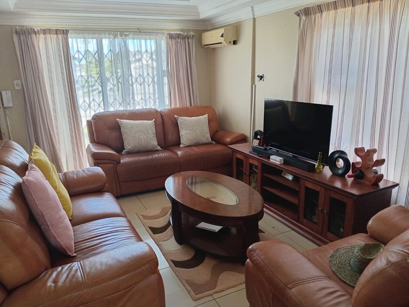 A comfortable living room featuring tiled flooring, decorative cornicing, and a wall-mounted air conditioning unit, with large windows providing natural light.