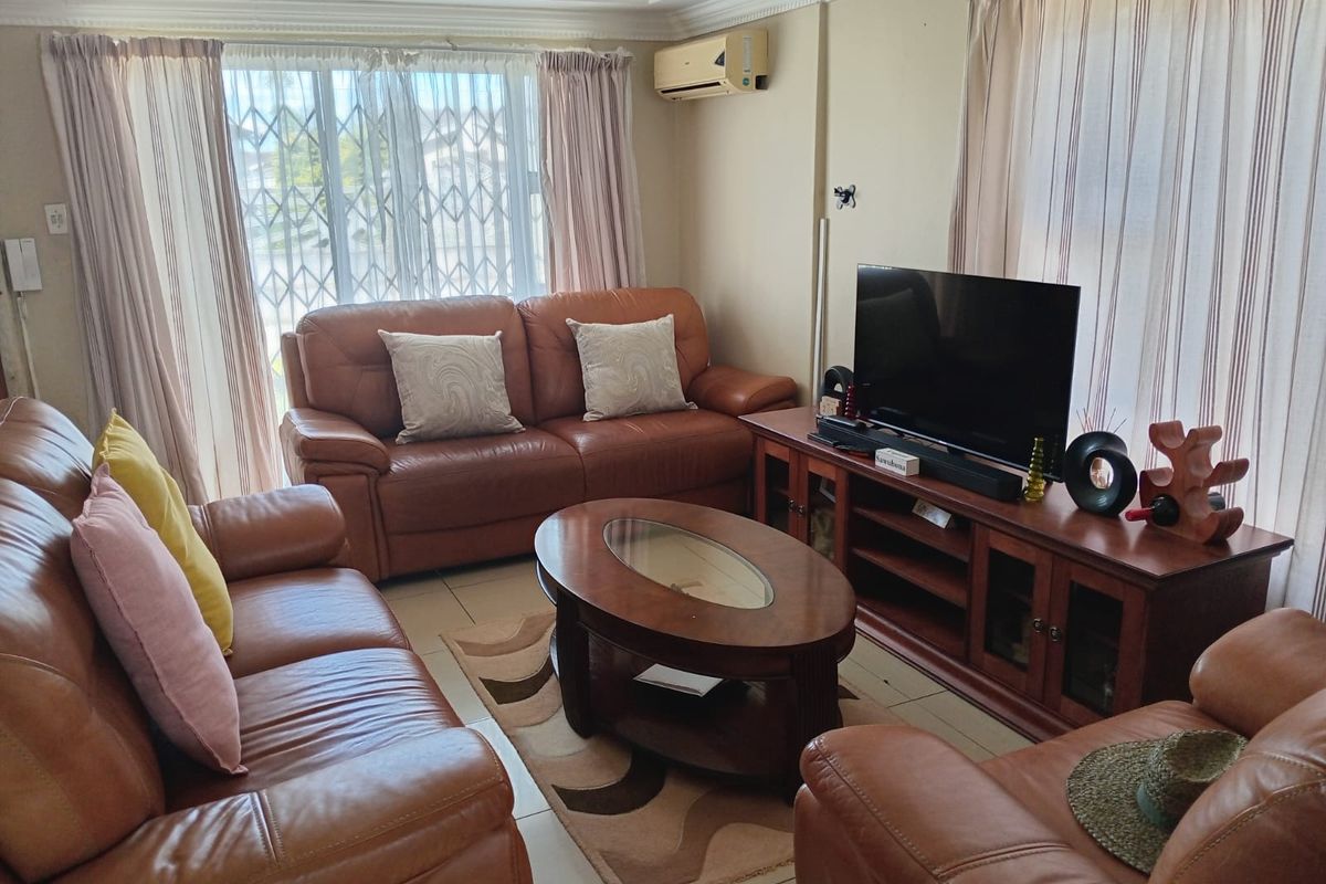 A comfortable living room featuring tiled flooring, decorative cornicing, and a wall-mounted air conditioning unit, with large windows providing natural light.