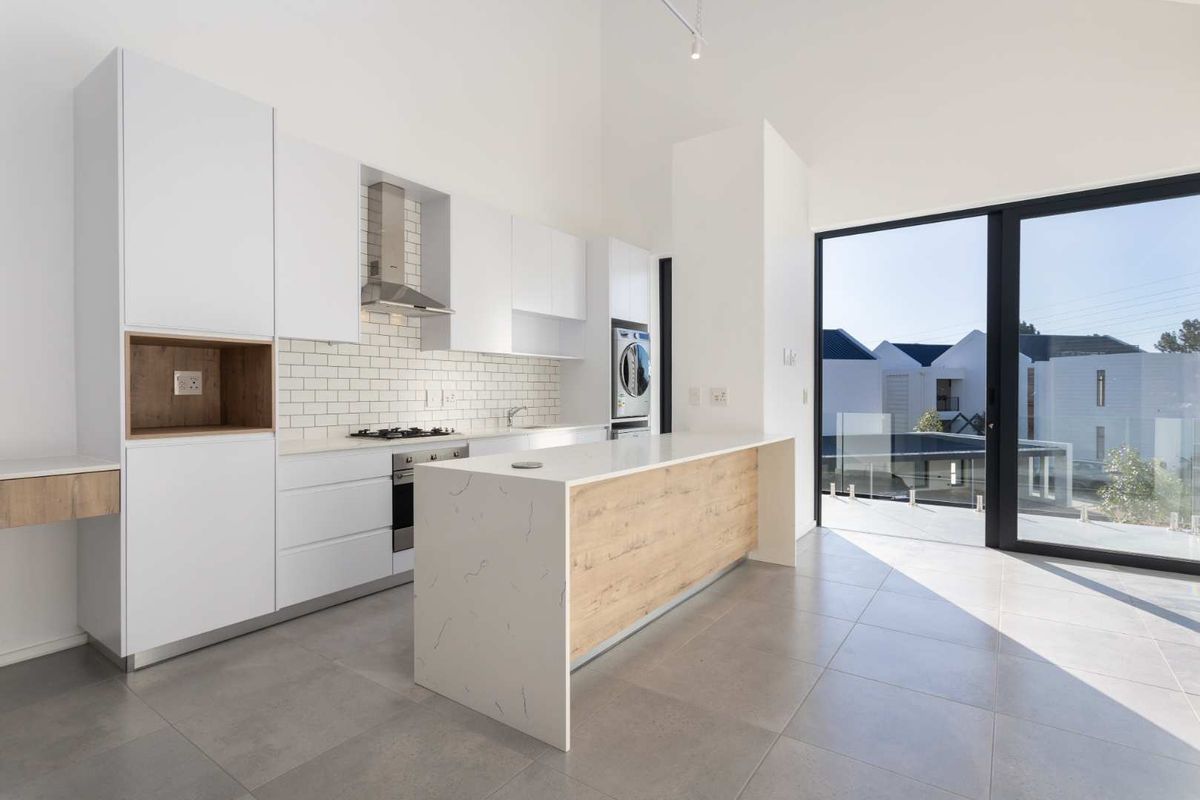 Modern open-plan kitchen featuring sleek white cabinetry, stone countertops, a central island, and direct access to a balcony through large sliding glass doors.