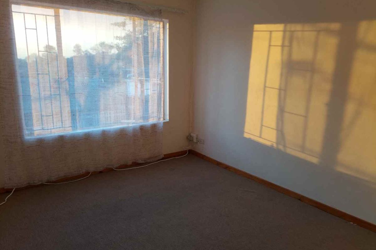 A vacant bedroom featuring neutral walls, carpeted flooring, and a large window with security bars, receiving ample natural light.