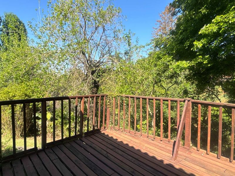 An elevated timber balcony featuring a wooden balustrade and views of the surrounding mature trees and greenery.