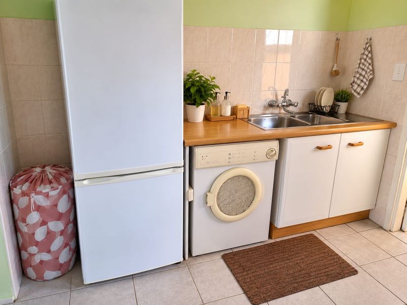 A functional laundry area featuring a stainless steel double sink, tiled backsplash, and built-in cabinetry with space for appliances.