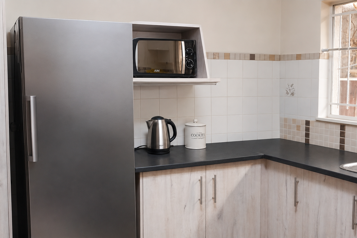 A functional kitchen area featuring light wood-grain cabinetry, dark countertops, a stainless steel sink, and a built-in microwave shelf.