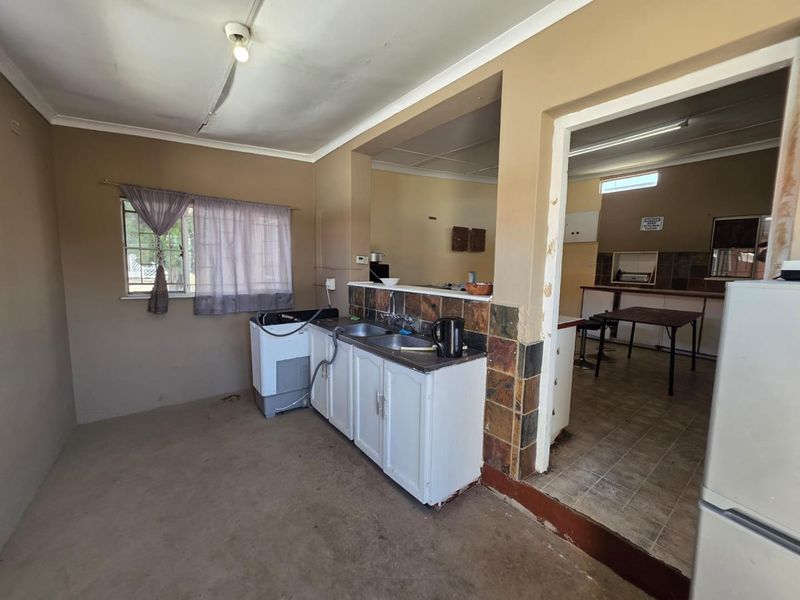 Open plan kitchen and utility area featuring built-in cabinetry, stone tile splashbacks, and a double sink, requiring cosmetic updates to modernize the space.