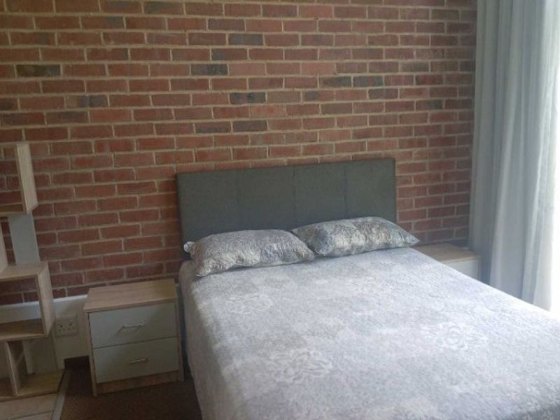 A bedroom featuring a prominent exposed brick feature wall and neutral flooring, offering a rustic aesthetic with natural light from the adjacent window.