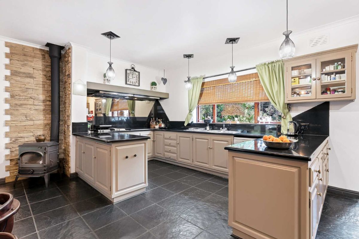 Spacious kitchen featuring dark stone countertops, custom cabinetry, a built-in wood-burning stove, and slate tile flooring.
