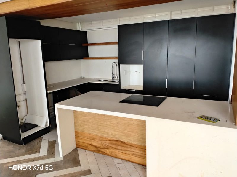 Modern kitchen featuring a central island with induction hob, matte black cabinetry, stone countertops, and stylish herringbone flooring in an open-plan layout.