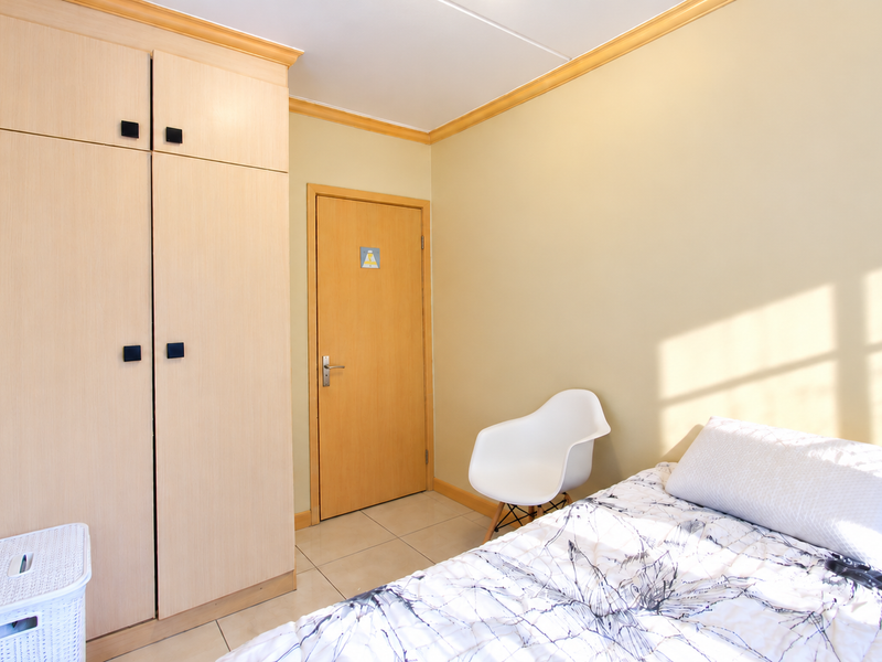 A well-maintained bedroom featuring light wood-toned built-in wardrobes, neutral wall paint, tiled flooring, and decorative crown molding.