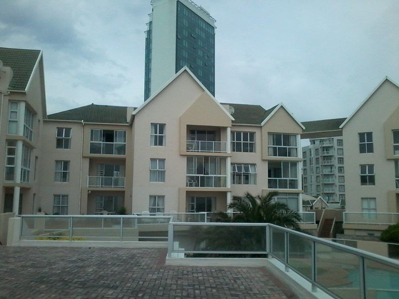 A view of the apartment complex rear elevation featuring multiple balconies with glass balustrades and a paved terrace area.
