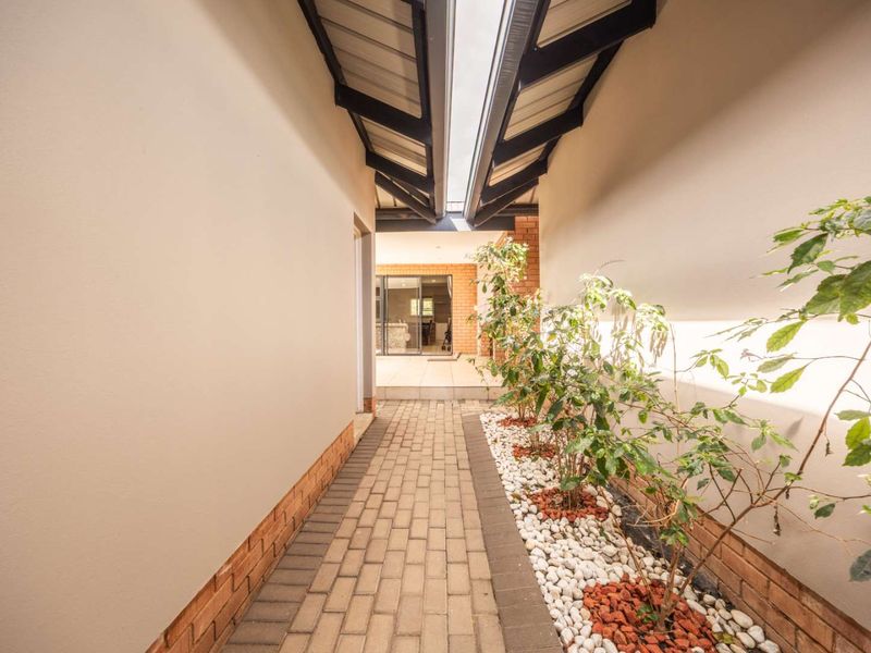 A covered outdoor walkway featuring brick paving, a central skylight, and a built-in brick planter bed leading toward the main living area.