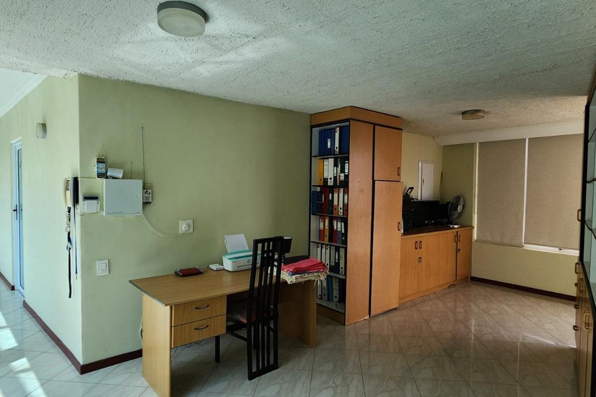 A functional home office space featuring built-in cabinetry, tiled flooring, and natural light from large windows.