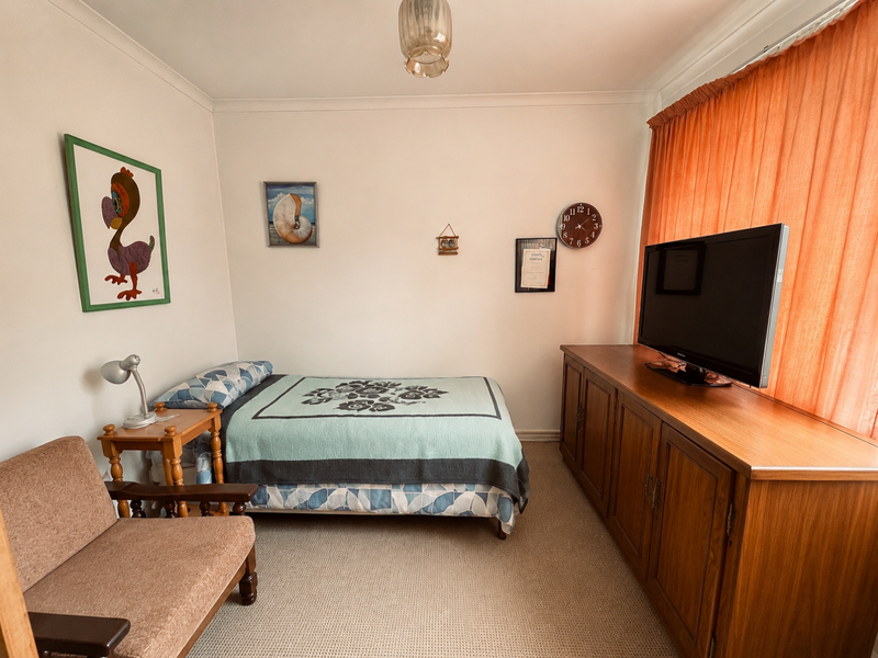 A functional bedroom featuring neutral carpet flooring, standard window treatments, and a central ceiling light fixture, offering a clean and well-maintained living space.