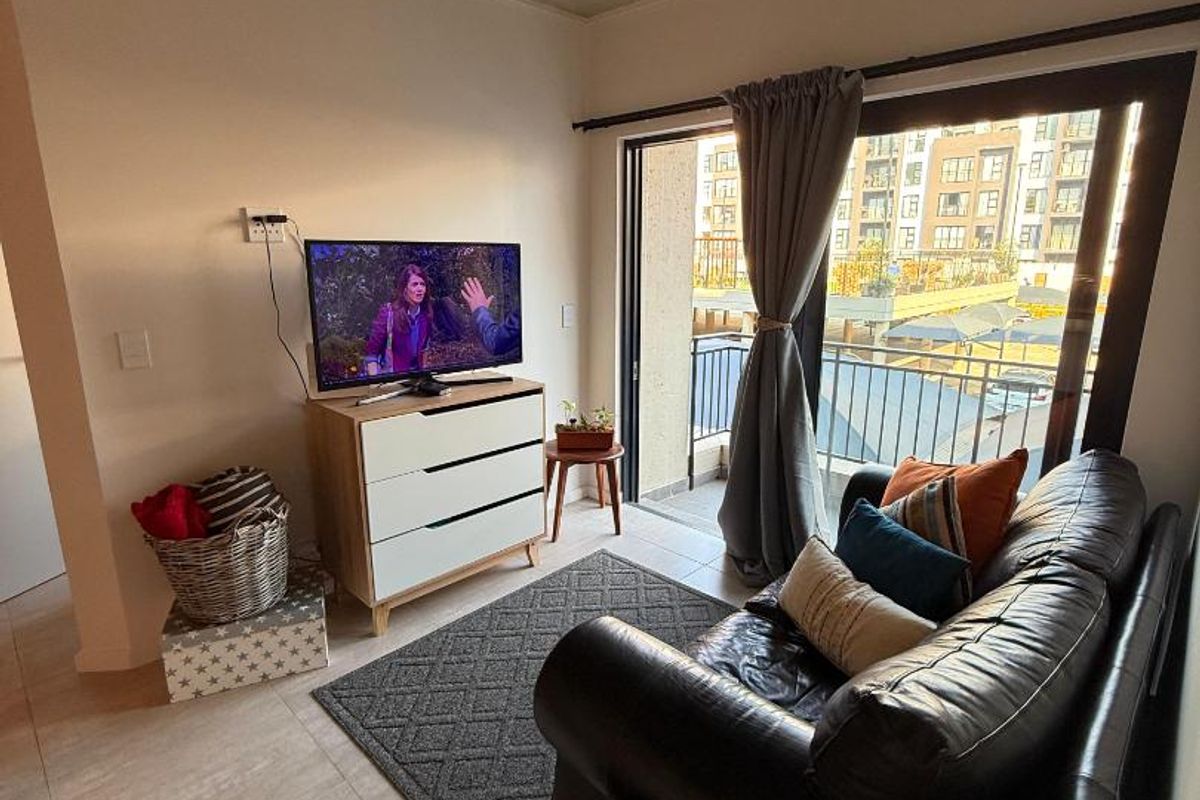 A cozy living room featuring tiled flooring, exposed concrete ceiling with track lighting, and sliding glass doors leading to a private balcony.