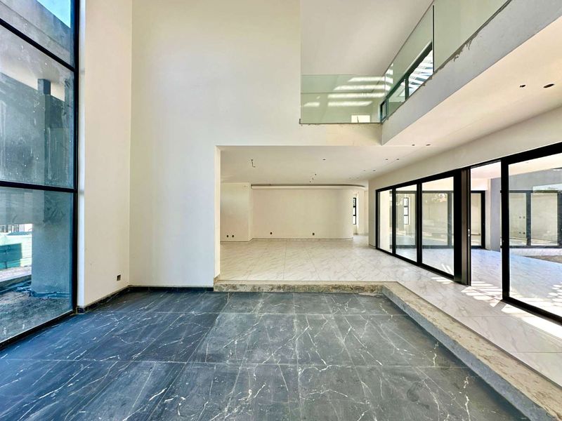 Spacious open-plan living area featuring double-volume ceilings, large format marble-look tiling, and extensive glass sliding doors leading to the exterior.