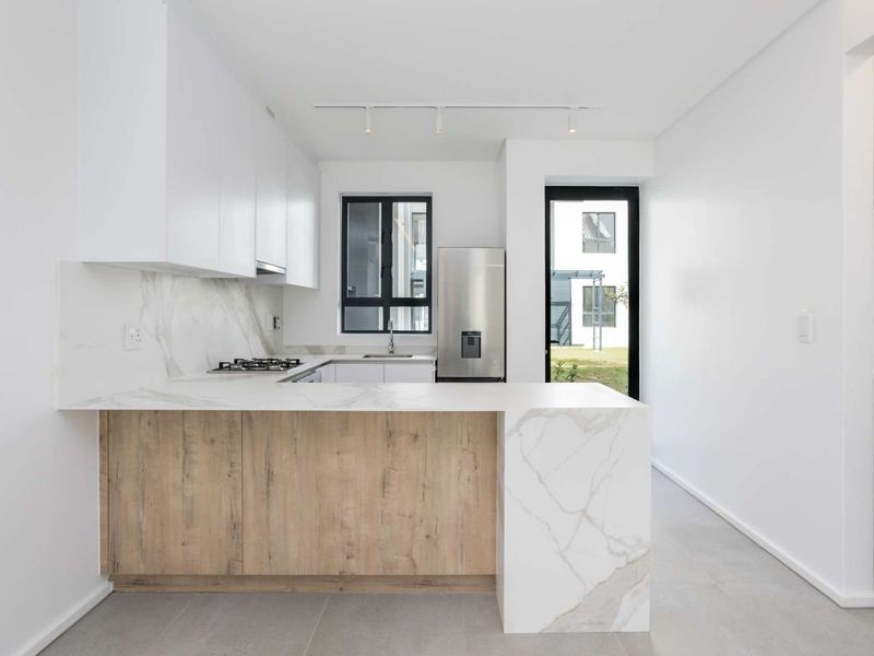 Modern kitchen featuring sleek white cabinetry, marble-look stone countertops, a gas hob, and integrated track lighting, offering a clean and contemporary aesthetic.