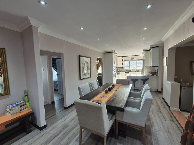 An open-plan dining and kitchen area featuring modern laminate flooring, recessed lighting, and a functional kitchen layout with built-in cabinetry and appliances.