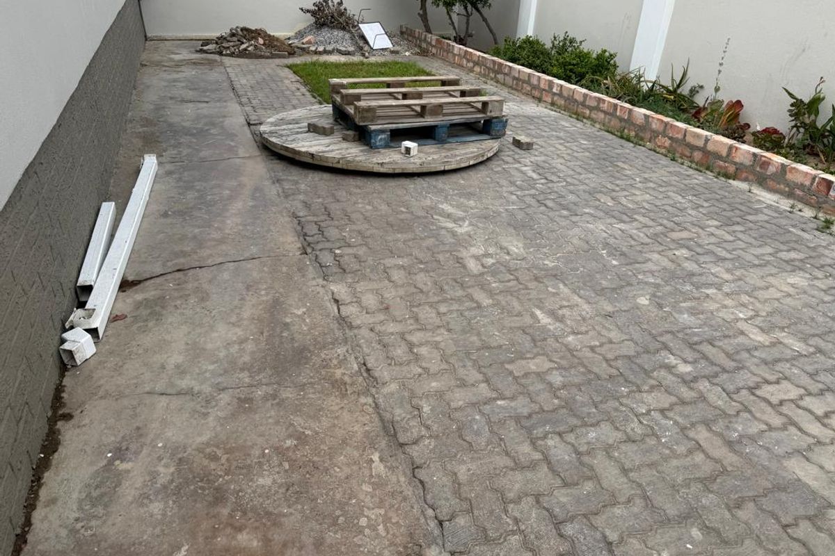 A paved rear courtyard area featuring a brick retaining wall and concrete sections, offering potential for landscaping or outdoor improvement.