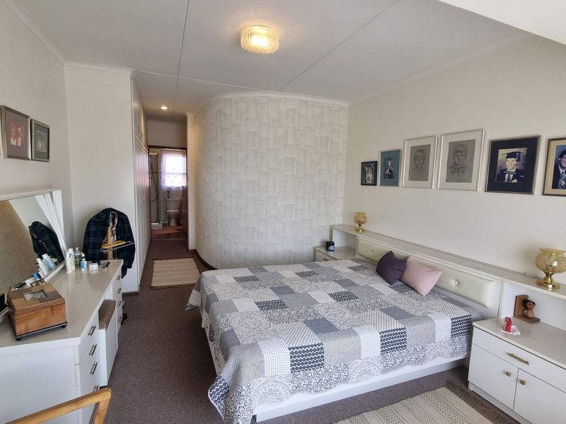 Spacious bedroom featuring a textured feature wall, built-in headboard with integrated shelving, and ample built-in cupboard storage, with an en-suite bathroom visible.