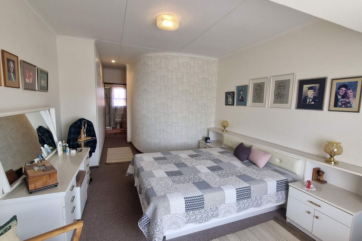 Spacious bedroom featuring a textured feature wall, built-in headboard with integrated shelving, and ample built-in cupboard storage, with an en-suite bathroom visible.