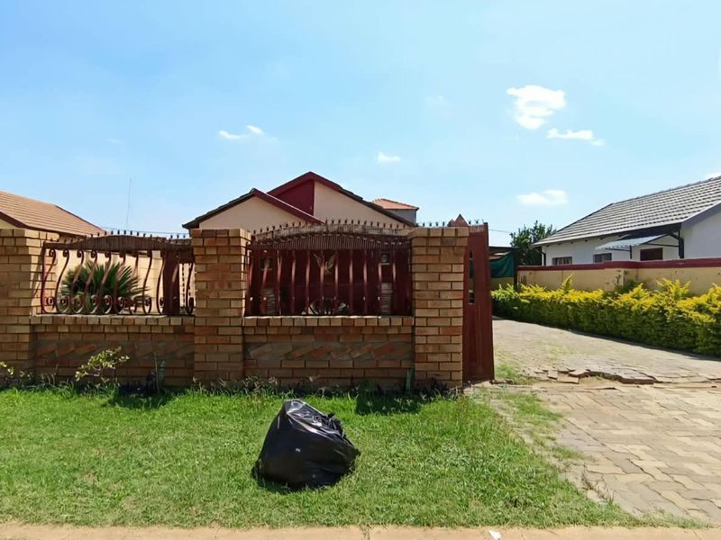 Front view of the property featuring a brick boundary wall with wrought iron fencing and a paved driveway entrance.