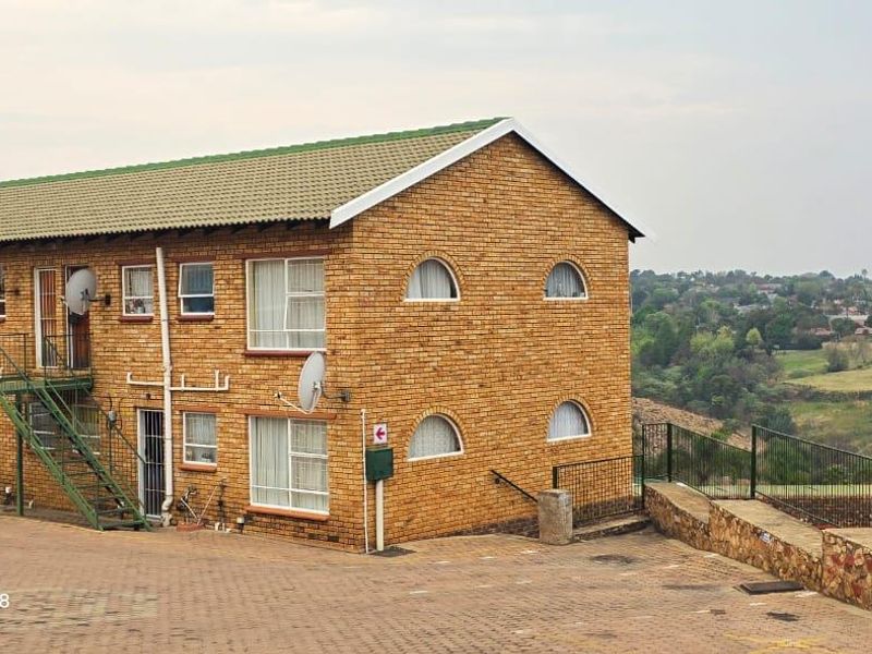 Exterior view of a face brick apartment building featuring a metal staircase, tiled roof, and paved driveway with surrounding landscape views.