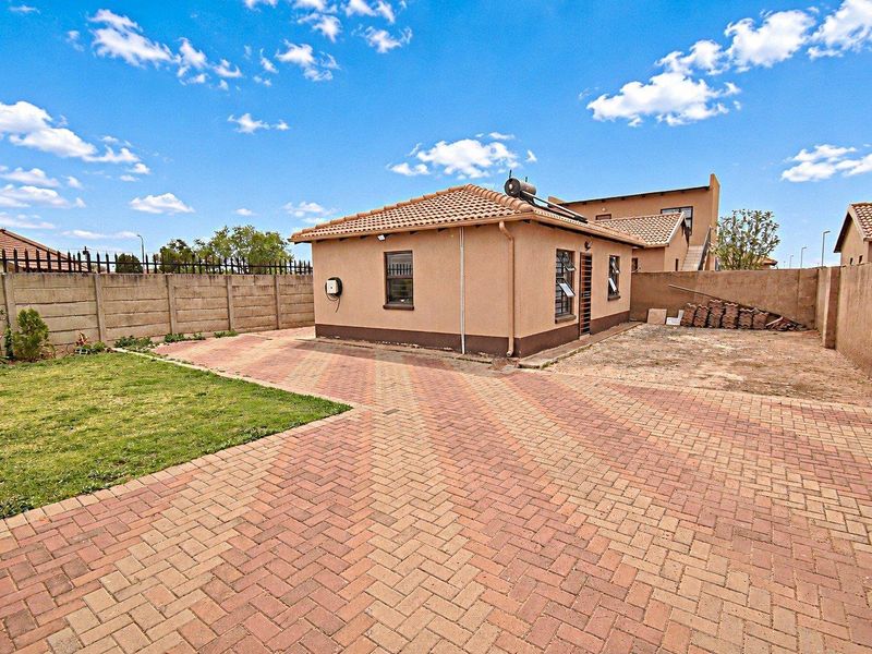 Rear exterior view of the property featuring a paved driveway, lawn area, and perimeter boundary wall with a solar water heater installed on the roof.