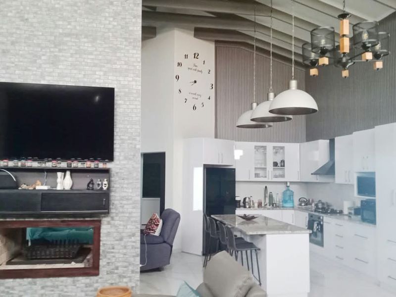 Spacious open-plan living and kitchen area featuring a stone-clad fireplace, high ceilings with exposed beams, and a modern kitchen with a central island.