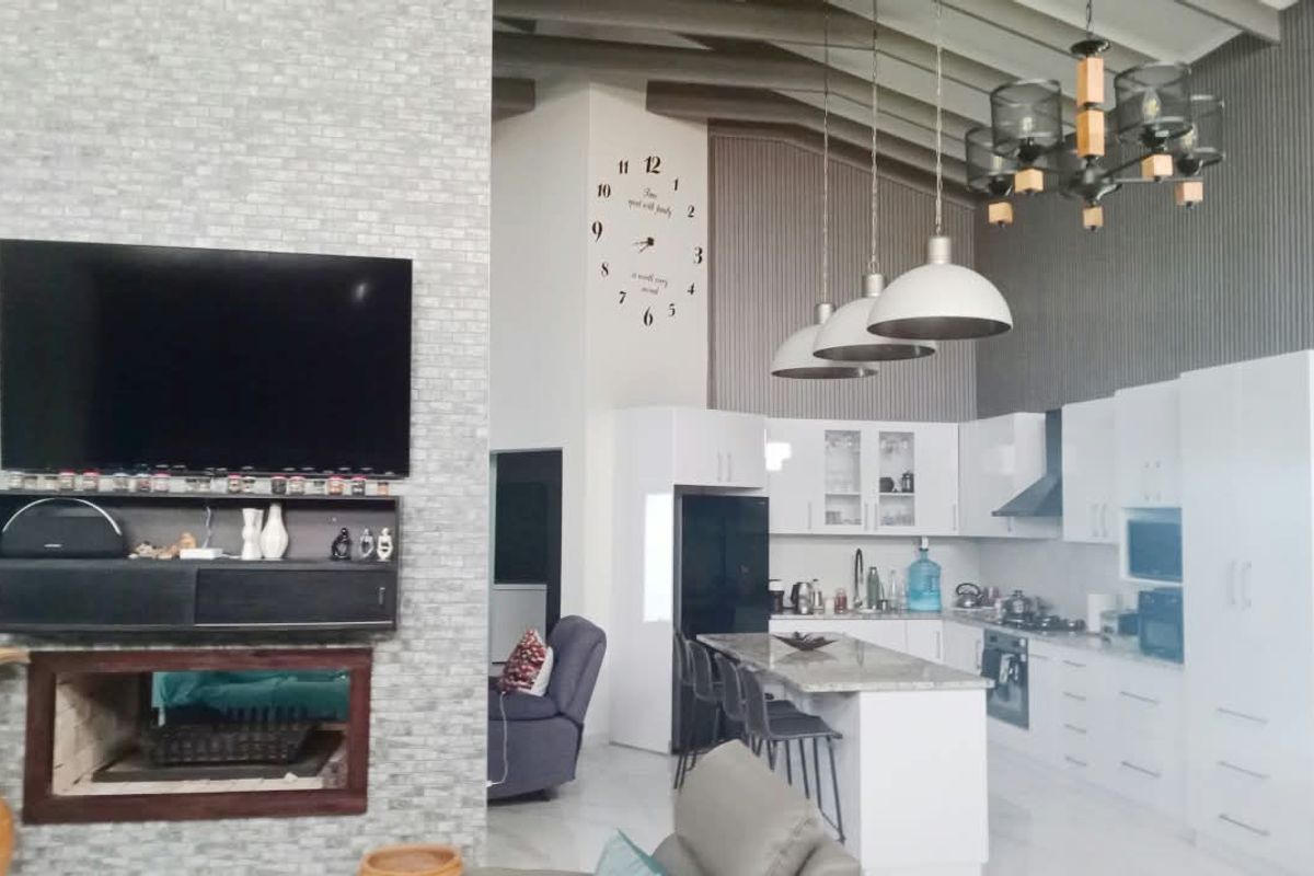 Spacious open-plan living and kitchen area featuring a stone-clad fireplace, high ceilings with exposed beams, and a modern kitchen with a central island.