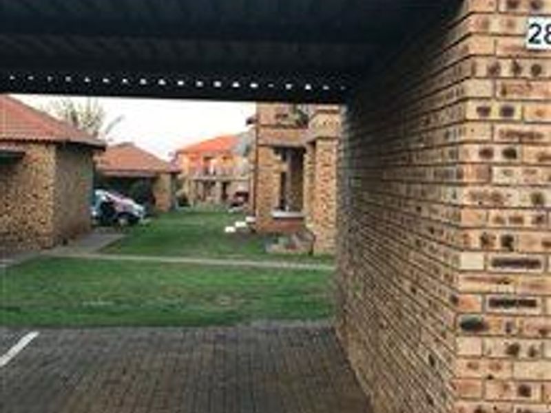 A view of the apartment complex exterior featuring a covered carport, face brick construction, and paved driveway access.