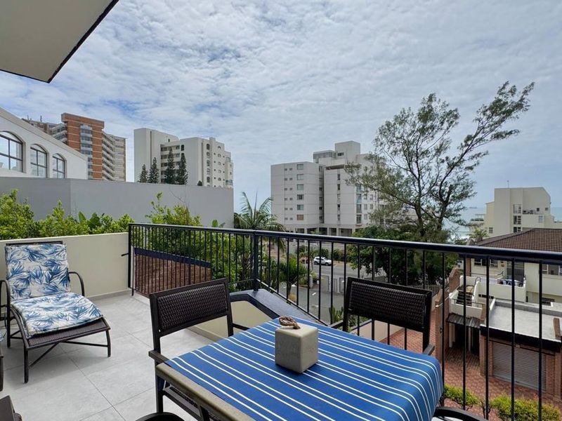 A spacious balcony featuring tiled flooring and a secure metal balustrade, offering an elevated outdoor area with urban and partial sea views.