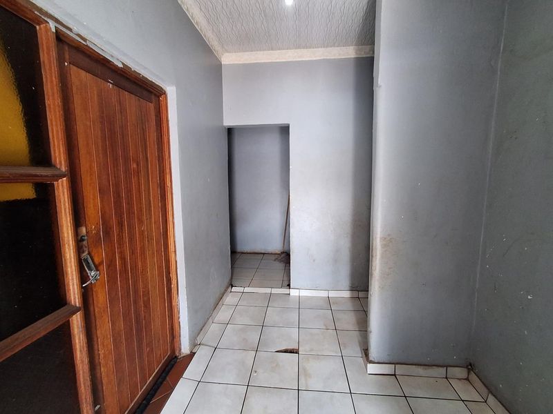 A vacant hallway featuring tiled flooring and a wooden door, showing signs of wear on the walls and floor tiles.