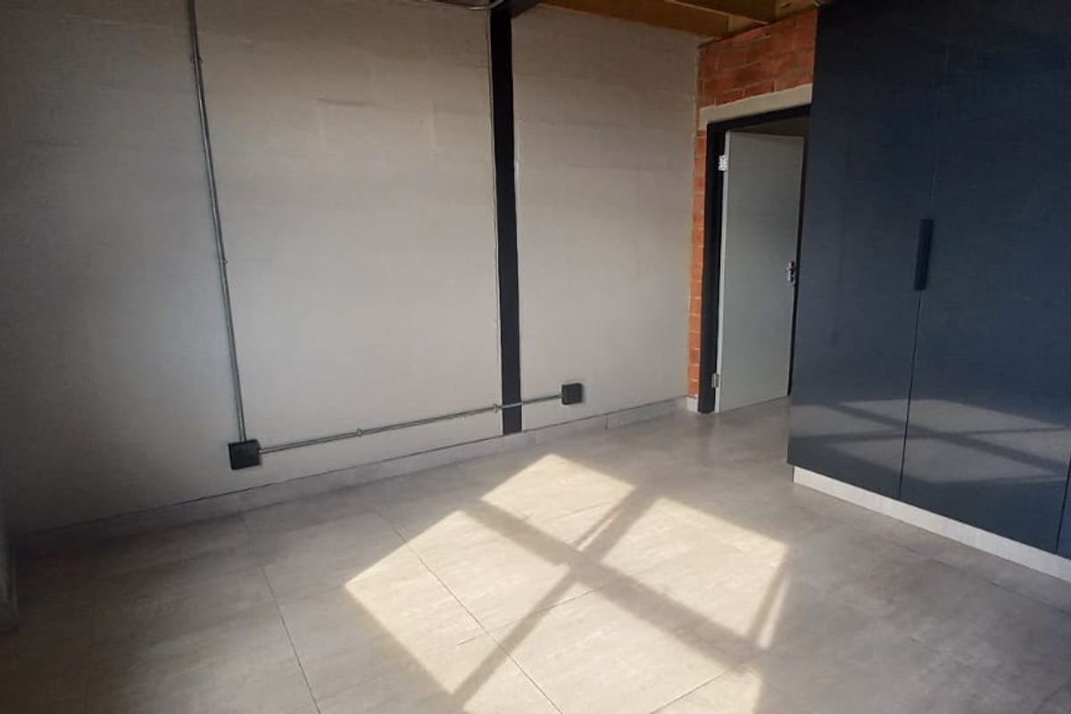 A compact bedroom featuring tiled flooring, built-in dark grey cabinetry, and an industrial aesthetic with exposed electrical conduit and brickwork accents.