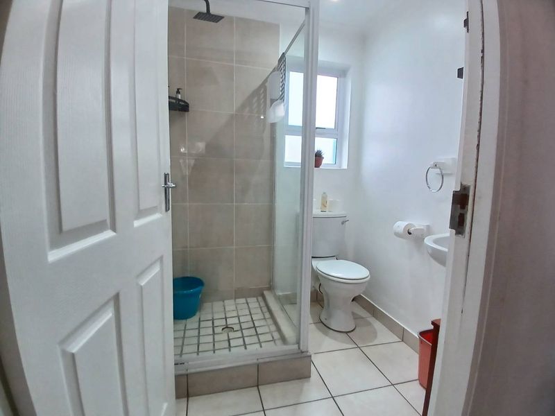 A compact bathroom featuring a tiled shower enclosure with a rain shower head, a standard toilet, and a wall-mounted basin.