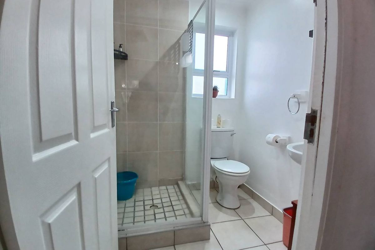 A compact bathroom featuring a tiled shower enclosure with a rain shower head, a standard toilet, and a wall-mounted basin.