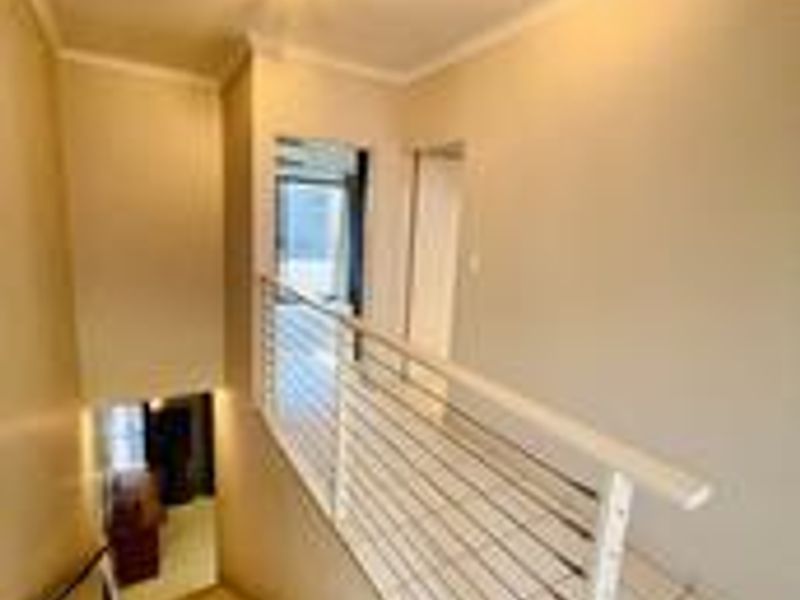 A bright hallway featuring a staircase with a modern metal balustrade and neutral tiled flooring, connecting different levels of the apartment.