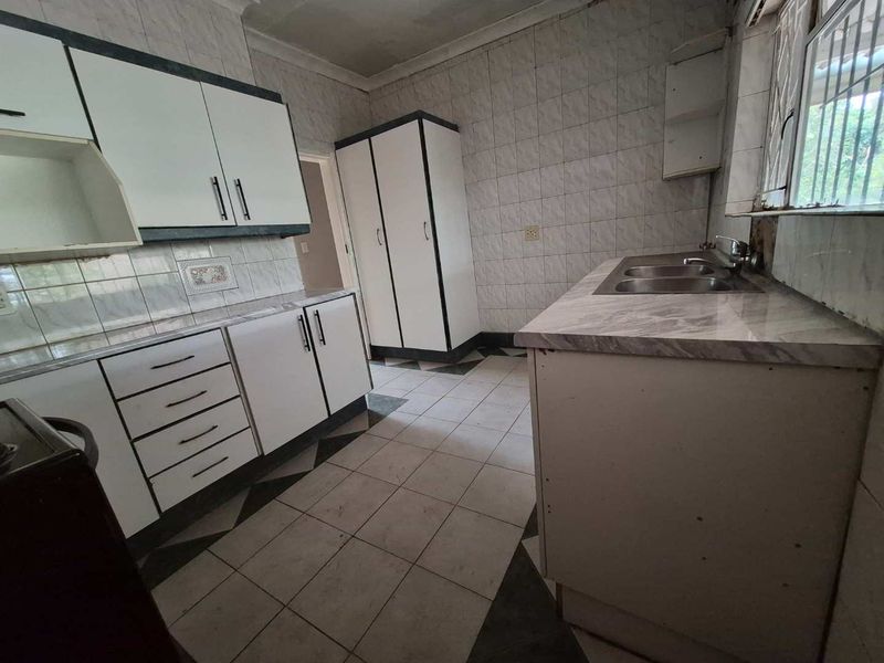 A dated kitchen featuring built-in cabinetry, laminate countertops, a double bowl sink, and tiled finishes throughout, offering potential for a modern renovation.