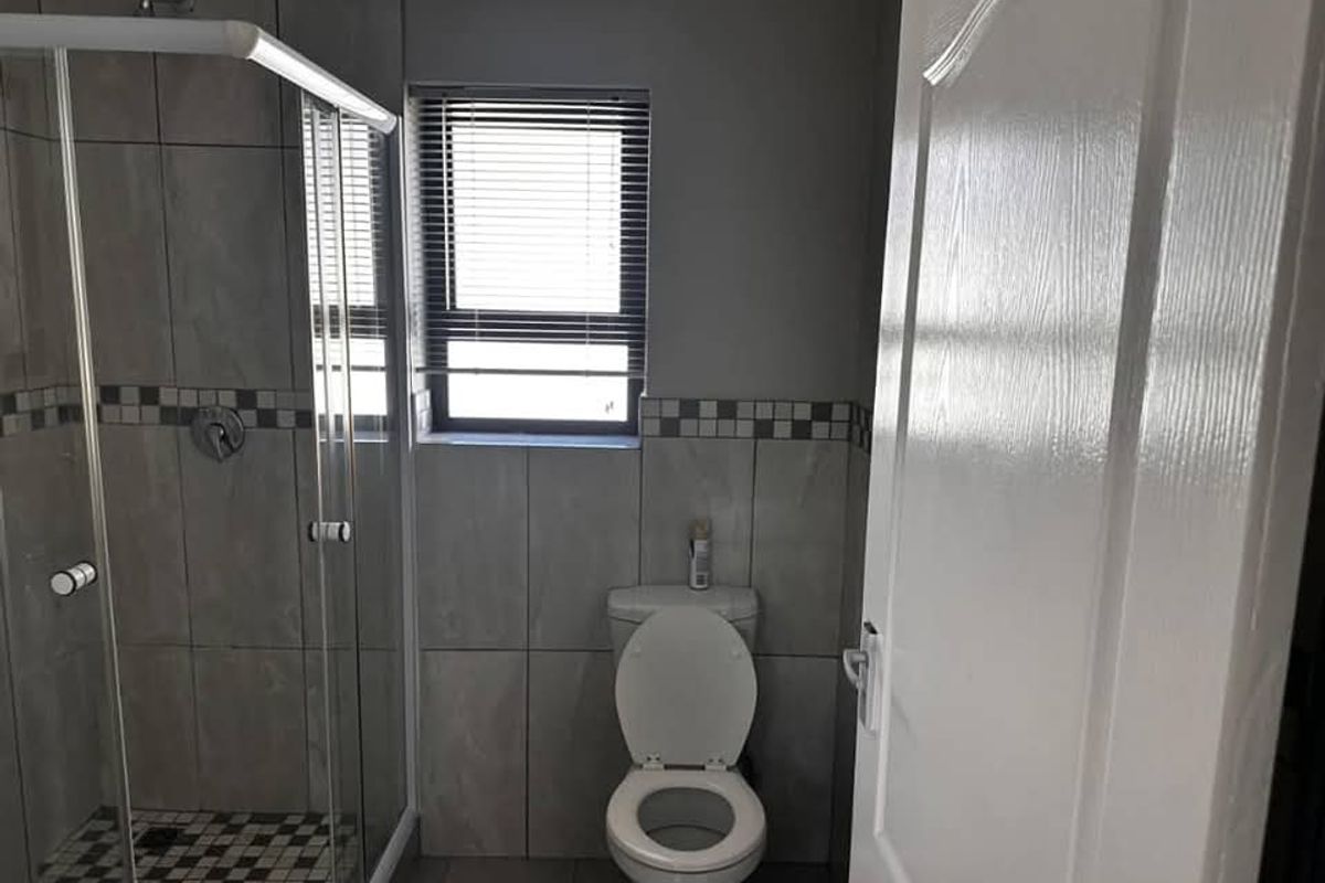 A functional bathroom featuring a glass-enclosed shower, tiled walls with decorative accents, and a standard toilet.