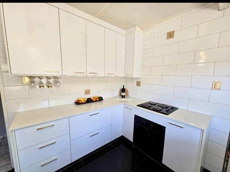Modern kitchen featuring white cabinetry, stone countertops, subway tile backsplash, built-in oven, and a black ceramic hob.
