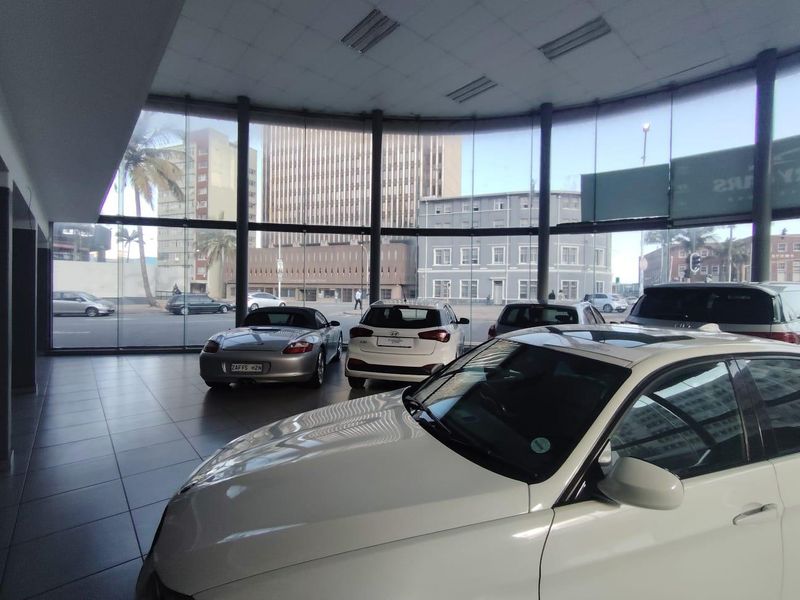 Spacious retail showroom featuring extensive floor-to-ceiling glass windows, tiled flooring, and recessed ceiling lighting, providing excellent visibility and natural light.