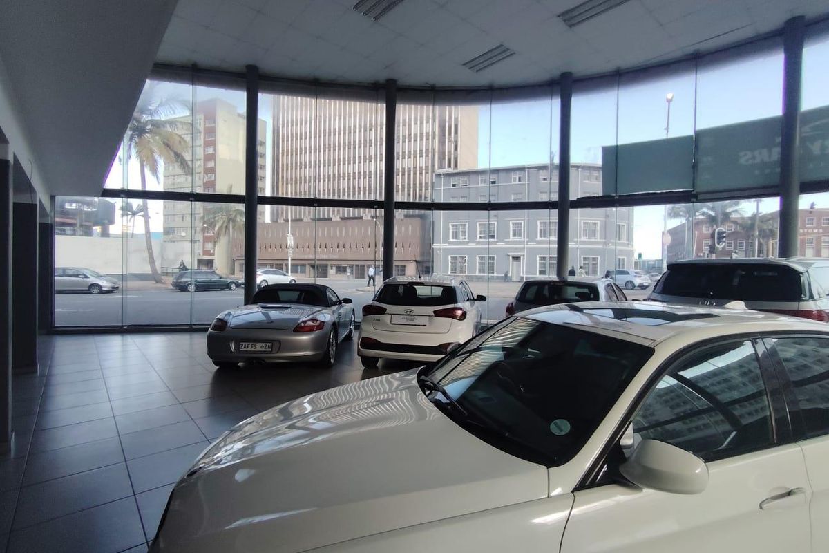 Spacious retail showroom featuring extensive floor-to-ceiling glass windows, tiled flooring, and recessed ceiling lighting, providing excellent visibility and natural light.