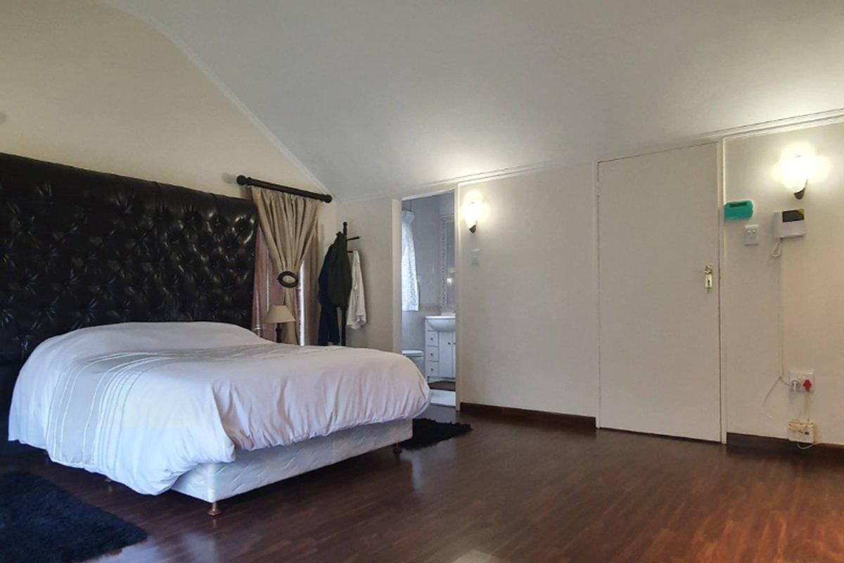 Spacious bedroom featuring vaulted ceilings, dark wood-look flooring, integrated wall lighting, and an en-suite bathroom access.