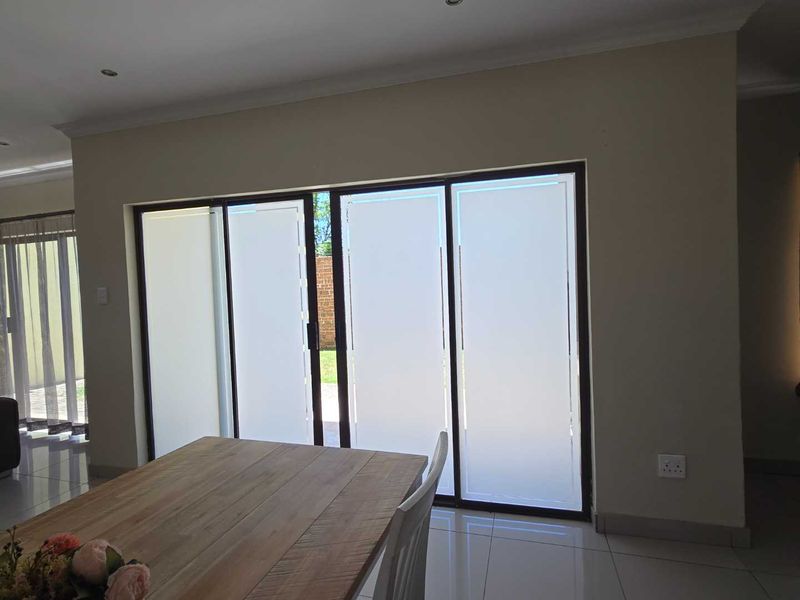 A bright living area featuring large sliding glass doors with privacy film, tiled flooring, and modern recessed lighting, providing seamless access to the outdoors.