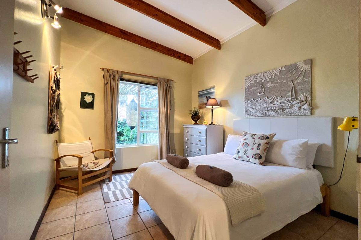 A cozy bedroom featuring exposed timber ceiling beams, tiled flooring, and a window overlooking the garden area.
