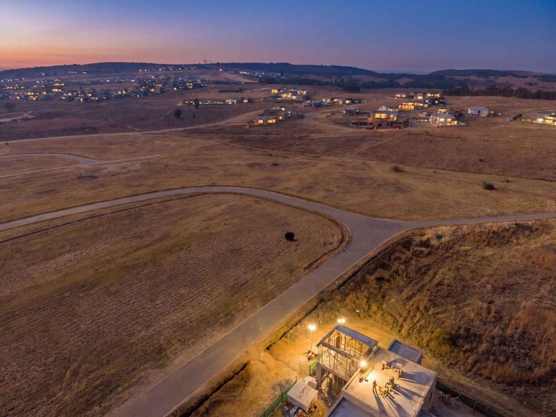 Aerial view of a residential development site at dusk, featuring paved roads and a structure currently under construction.